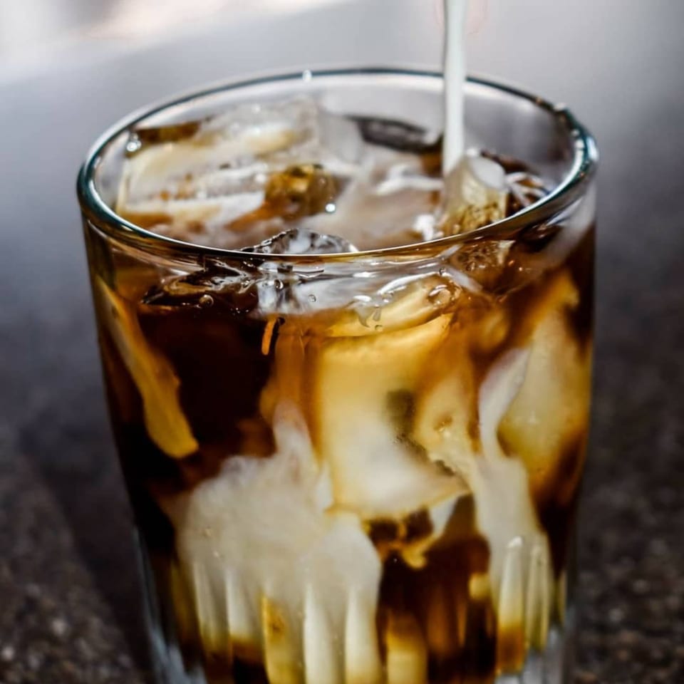 Creamy white milk being poured into a glass of iced coffee, creating swirls of brown and white.