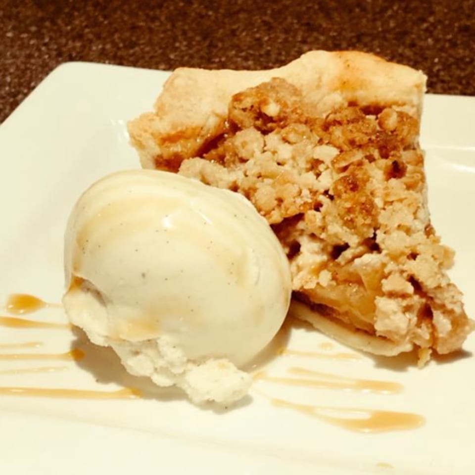 A slice of apple crumble pie with a scoop of vanilla ice cream and caramel drizzle.