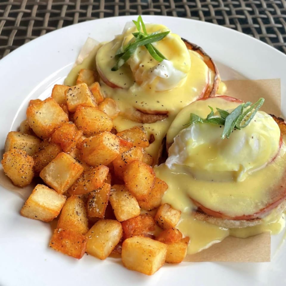 Two servings of Eggs Benedict with hollandaise sauce and a side of crispy home fries.