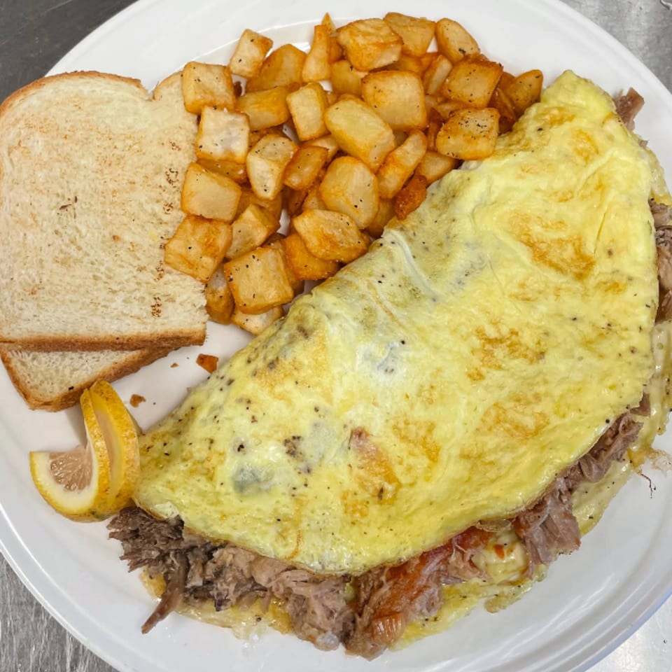 A Menehune Coffee Company omelet filled with meat, served with home fries, toast, and lemon wedges.