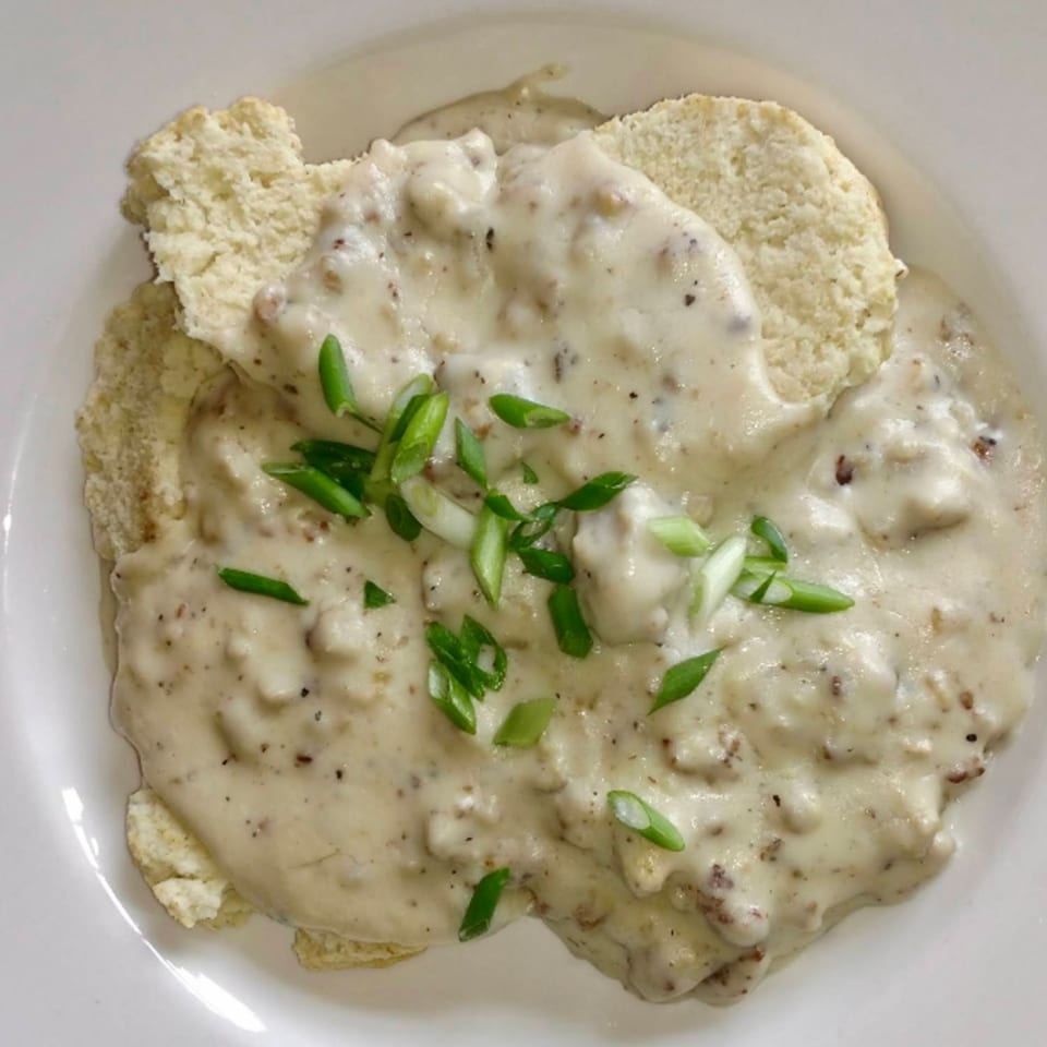 Biscuits and gravy, topped with chopped green onions, served on a white plate.