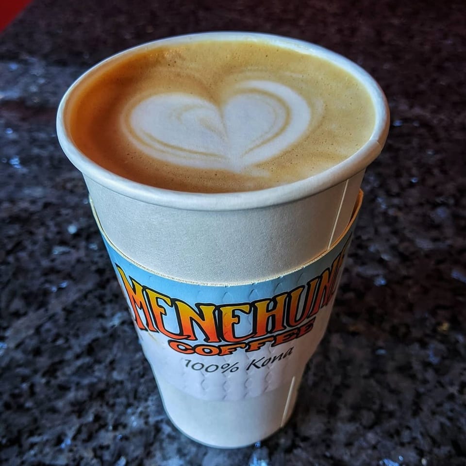 A Menehune Coffee Company cup of latte with a heart design in the foam.