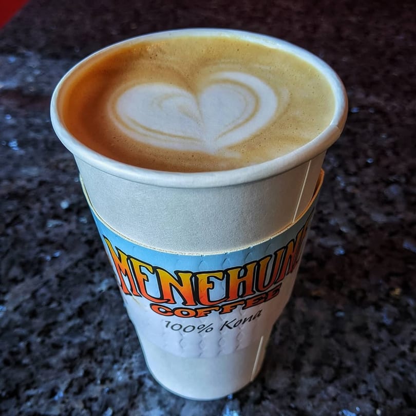 A Menehune Coffee Company cup of latte with a heart design in the foam.